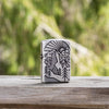 Lifestyle image of Armor® Antique Silver Mountain Design Windproof Lighter standing on a wooden surface with woods blurred in the background