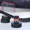 Lifestyle image of the NHL® Edmonton Oilers™ Street Chrome™ Windproof Lighter standing with a hockey puck and hockey stick, with a hockey net in the background.