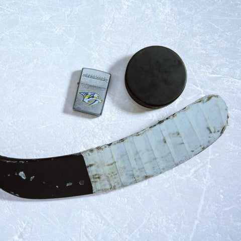 Lifestyle image of the NHL® Nashville Predators® Street Chrome™ Windproof Lighter laying on ice with a hockey puck and stick