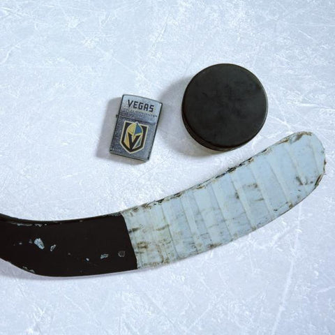 Lifestyle image of the NHL® Vegas Golden Knights™ Street Chrome™ Windproof Lighter laying on ice with a hockey puck and stick