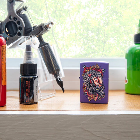 Lifestyle image of Wolf in Sheep's Clothing Design Purple Matte Windproof Lighter standing on a window sill with a tattoo gun and ink bottles