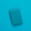 Lifestyle image of Classic Flat Turquoise Windproof Lighter laying on a turquoise surface