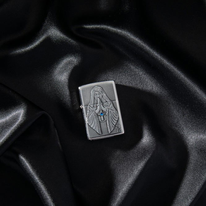 Lifestyle image of Anne Stokes Gothic Prayer Emblem Brushed Chrome Windproof Lighter laying on black silk.