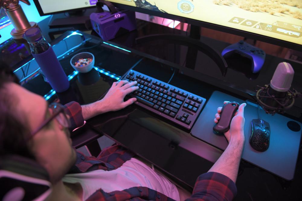 Lifestyle image of Black Heatbank 9s Gaming hand warmer in hand with a mouse and keyboard