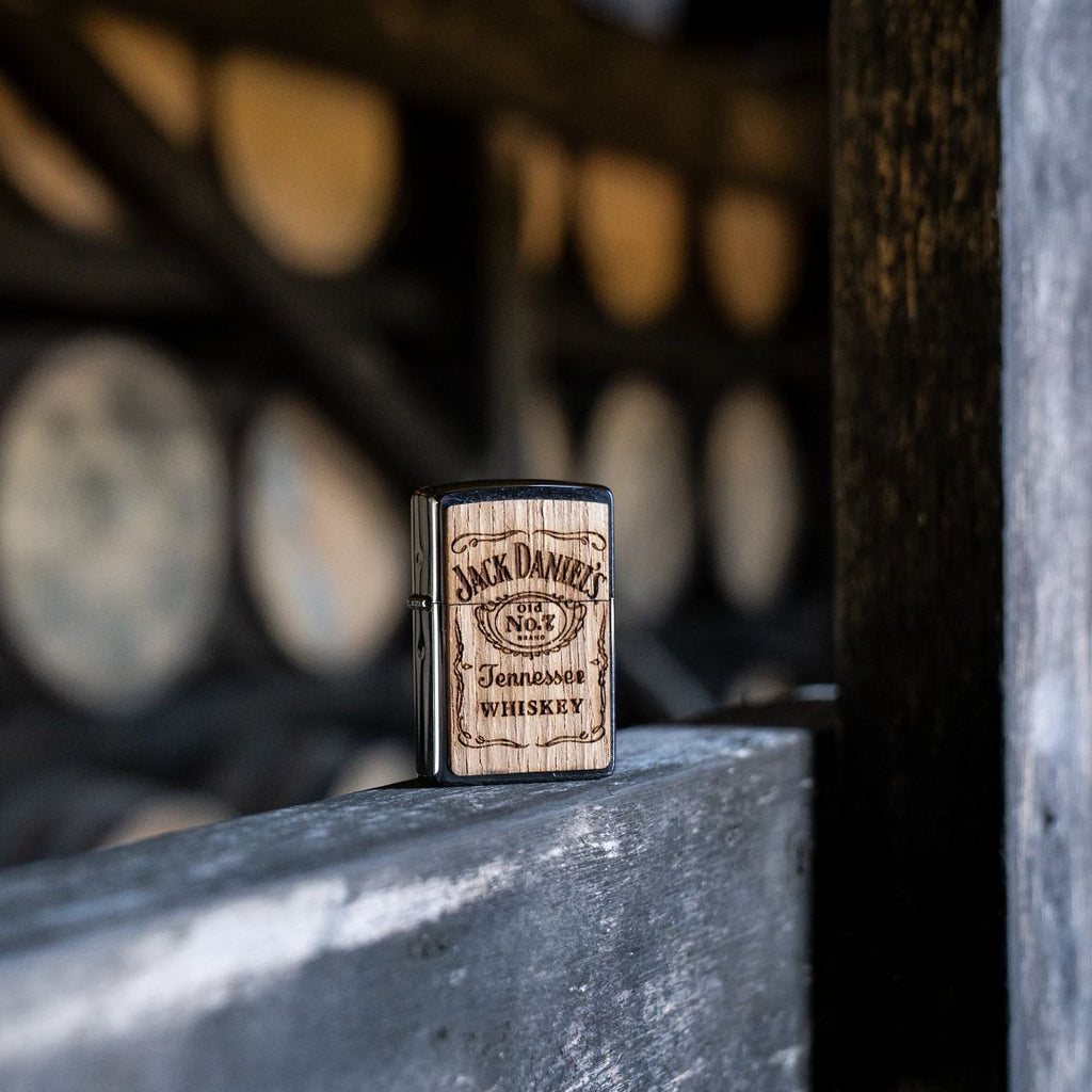 Lifestyle image of Jack Daniels WOODCHUCK USA Lighter standing on a wooden beam with whiskey barrels in the background.