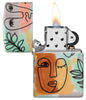 Abstract Faces Design 540 Color Windproof Lighter lit in hand.