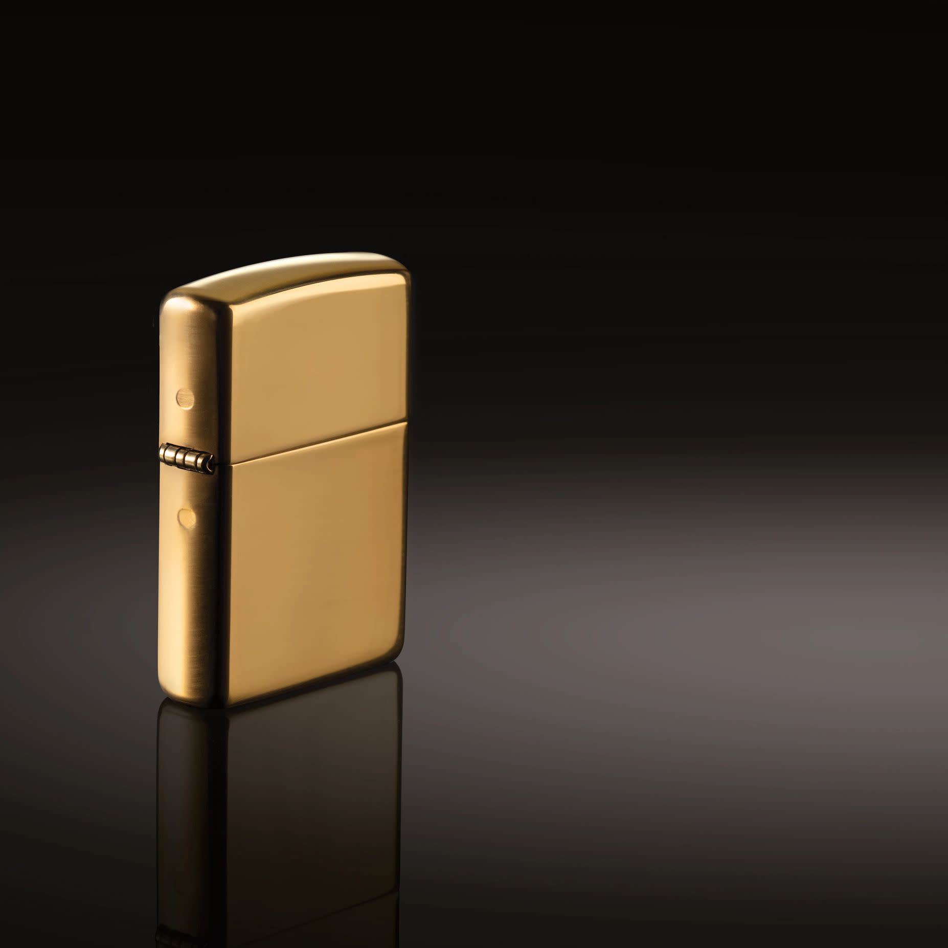 Lifestyle image of ArmorÂ® High Polish 18K Solid Gold Windproof Lighter standing in a black background.