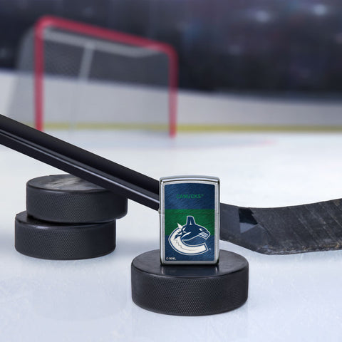 Lifestyle image of the NHL® Vancouver Canucks™ Street Chrome™ Windproof Lighter standing with a hockey puck and hockey stick, with a hockey net in the background.