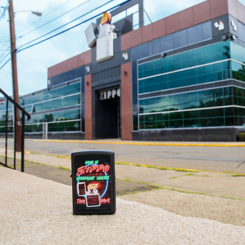 Lifestyle image of Neon Sign Design Black Matte Windproof Lighter standing in front of the Zippo building.