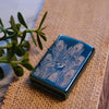 Lifestyle image of Peacock Design High Polish Teal Windproof Lighter laying on a table with a plant
