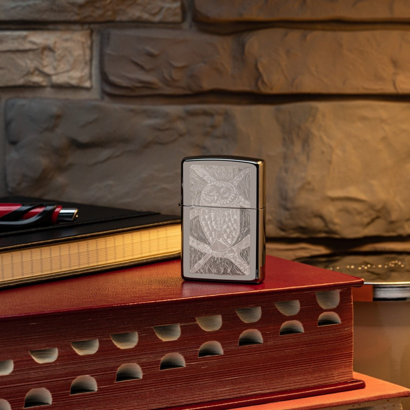Lifestyle image of John Smith Gumbula Bird High Polish Teal Windproof Lighter standing on a red book with glasses laying next to it
