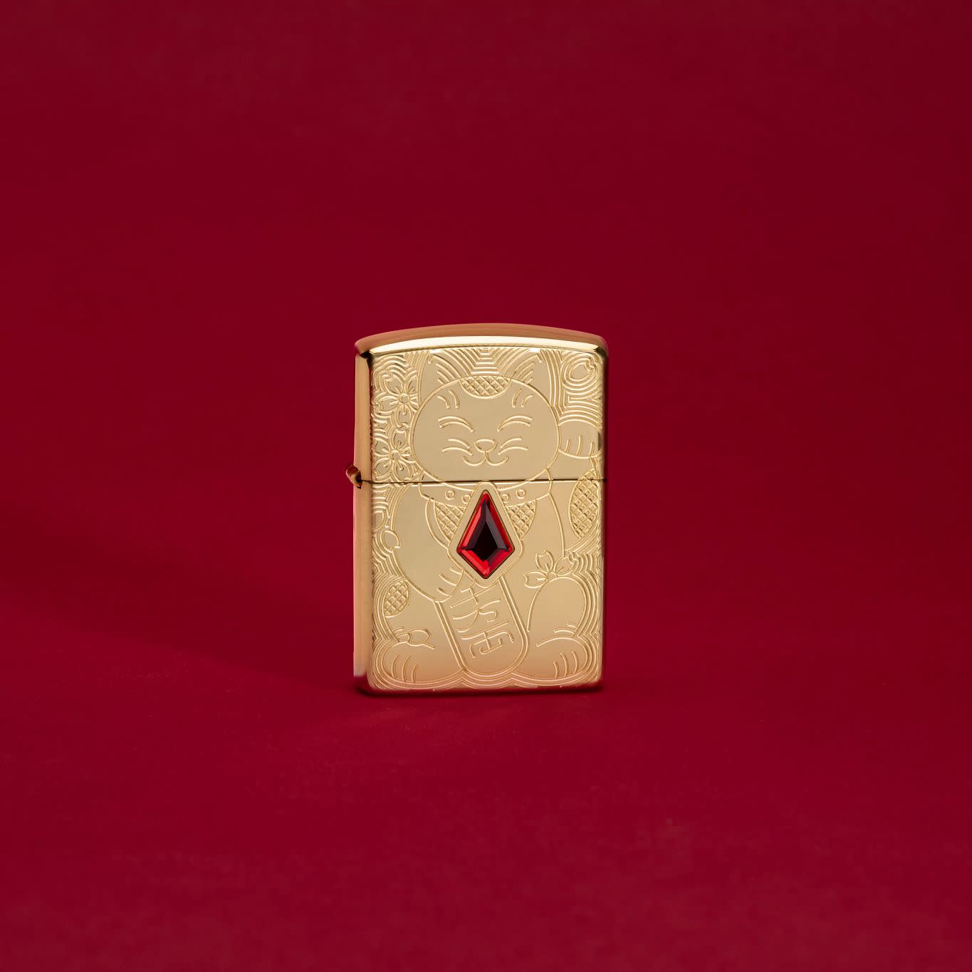 Lifestyle image of Lucky Cat Design Emblem Attached ArmorÂ® High Polish Brass Windproof Lighter standing in a red scene.