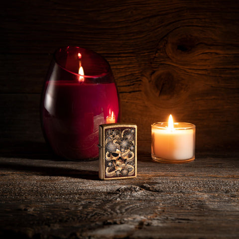 Lifestyle image of Snake Bouquet Design Tumbled Brass Windproof Lighter standing in a dark scene with a lit candle.