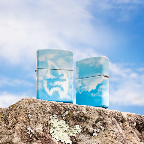 Lifestyle image of two Cloudy Sky Design 540 Color Windproof Lighters standing on a rock with clouds in the background.