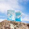 Lifestyle image of two Cloudy Sky Design 540 Color Windproof Lighters standing on a rock with clouds in the background.