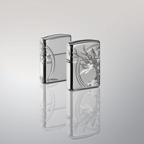 Lifestyle image of two Armor® High Polish Sterling Silver Tree of Life Windproof Lighters standing in a silver mirror scene. One lighter is showing the front of the design with the other showing the back.