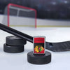 Lifestyle image of the NHL® Chicago Blackhawks™ Street Chrome™ Windproof Lighter standing with a hockey puck and hockey stick, with a hockey net in the background.
