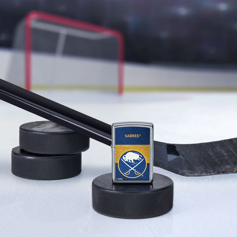 Lifestyle image of the NHL® Buffalo Sabre Street Chrome™ Windproof Lighter standing with a hockey puck and hockey stick, with a hockey net in the background.