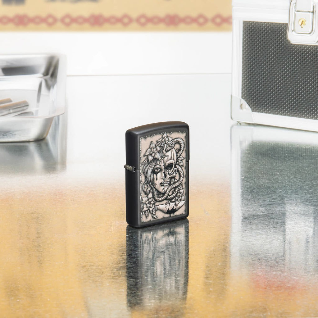 Lifestyle shot of Zippo Gory Tattoo Design Black Matte Windproof Lighter standing in on a reflective table with tattoo equipment.