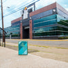 Lifestyle image of Windy Design High Polish Teal Windproof Lighter standing in front of the Zippo building.
