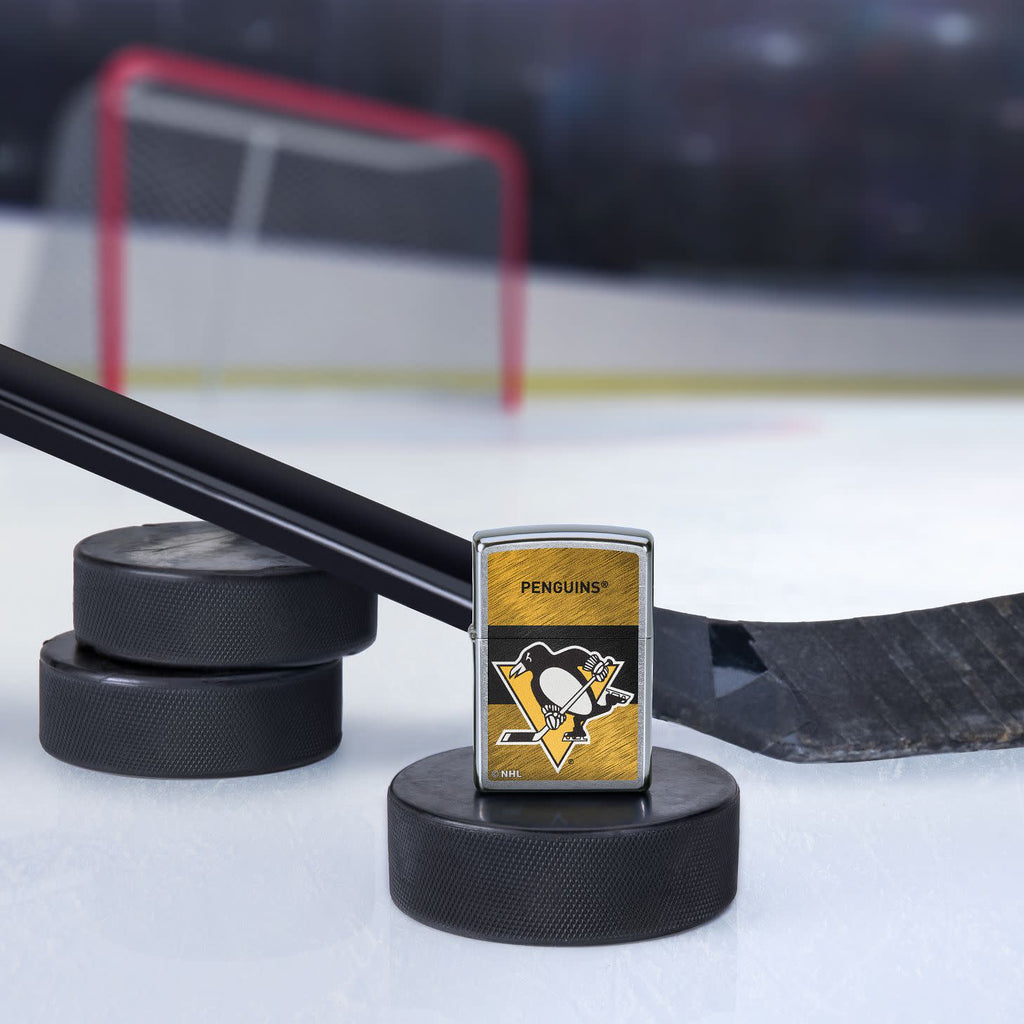 Lifestyle image of the NHL® Pittsburgh Penguins™ Street Chrome™ Windproof Lighter standing with a hockey puck and hockey stick, with a hockey net in the background.