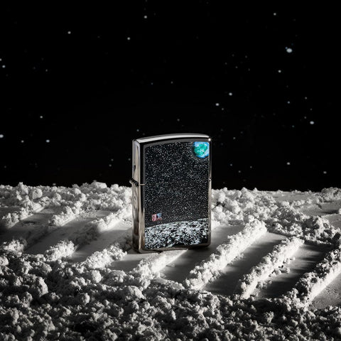 Front view of the High Polish Chrome Moon Landing Design Lighter shot with a galaxy background, sitting in gray sand 