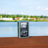 Lifestyle image of Mountain Lion Design Street Chrome Windproof Lighter standing on a railing with a lake behind it.