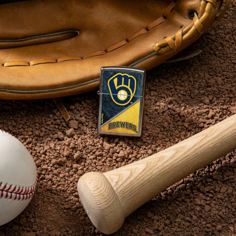 Lifestyle image of MLB™ Milwaukee Brewers™ Street Chrome™ Windproof Lighter laying on a baseball field with a glove, ball, and bat.