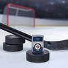 Lifestyle image of the NHL® Winnipeg Jets™ Street Chrome™ Windproof Lighter standing with a hockey puck and hockey stick, with a hockey net in the background.