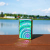 Lifestyle image of Cannabis Leaf Design Multi Color Windproof Lighter standing on a railing with a lake behind it.