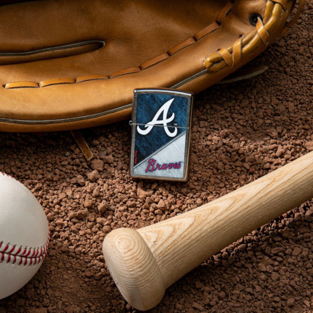 Lifestyle image of MLB™ Atlanta Braves™ Street Chrome™ Windproof Lighter laying on a baseball field with a glove, ball, and bat.