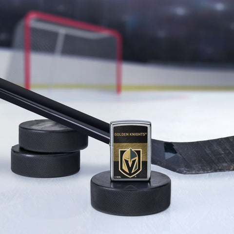 Lifestyle image of the NHL® Vegas Golden Knights™ Street Chrome™ Windproof Lighter standing with a hockey puck and hockey stick, with a hockey net in the background.