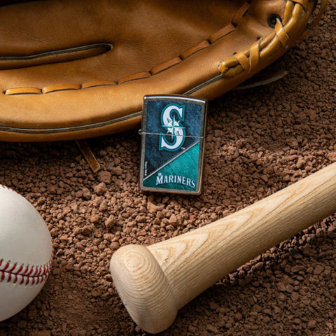 Lifestyle image of MLB™ Seattle Mariners™ Street Chrome™ Windproof Lighter laying on a baseball field with a glove, ball, and bat.