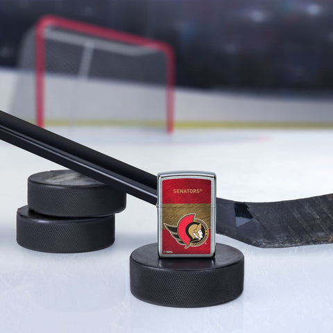 Lifestyle image of the NHL® Ottawa Senators™ Street Chrome™ Windproof Lighter standing with a hockey puck and hockey stick, with a hockey net in the background.