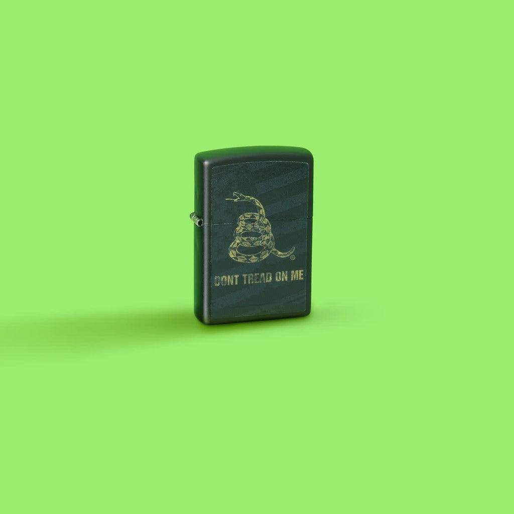 Glamour shot of Zippo Don't Tread On Me Snake and Flag Black Matte Windproof Lighter standing in a green scene.