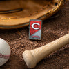 Lifestyle image of MLB® Cincinnati Reds™ Street Chrome™ Windproof Lighter laying on a baseball field with a glove, ball, and bat.