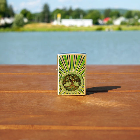 Lifestyle image of Fusion Tree of Life Design High Polish Brass Windproof Lighter standing on a railing with a lake behind it.