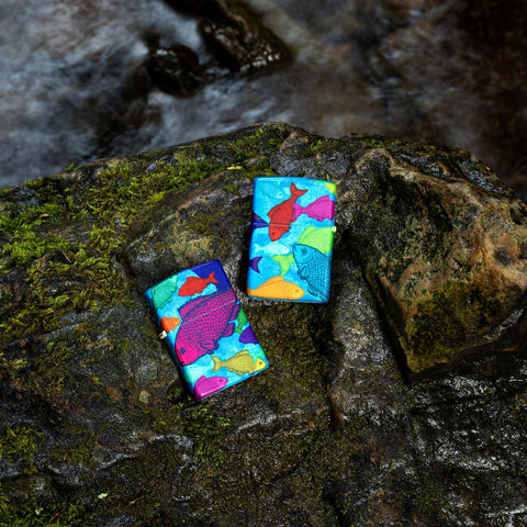 Lifestyle image of two Fishy Design 540 Color Windproof Lighters laying on a wet rock.