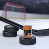 Lifestyle image of the NHL® Philadelphia Flyers™ Street Chrome™ Windproof Lighter standing with a hockey puck and hockey stick, with a hockey net in the background.