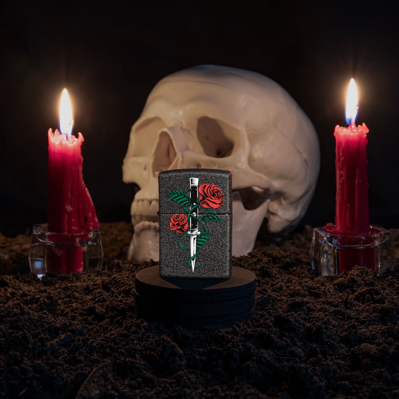 Lifestyle image of Rose Dagger Tattoo Design Black CrackleÂ® Windproof Lighter standing with a skull and lit candles behind it.