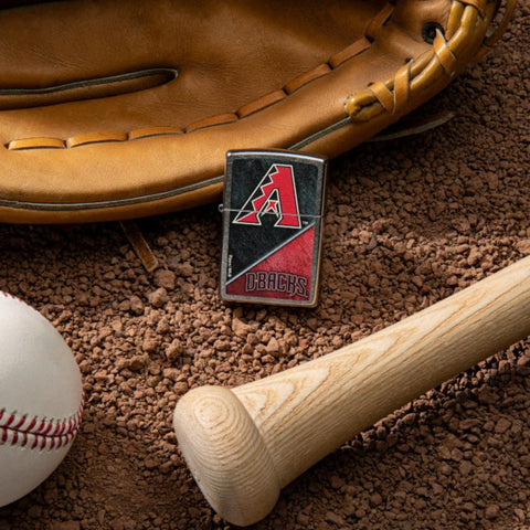 Lifestyle image of MLB™ Arizona Diamondbacks™ Street Chrome™ Windproof Lighter laying on a baseball field with a glove, ball, and bat.