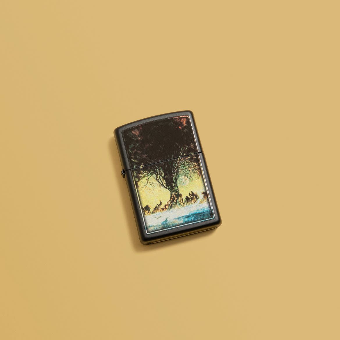 Lifestyle image of Frank Frazetta Tree Design Black Matte Windproof Lighter laying on a yellow background.