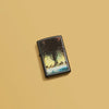 Lifestyle image of Frank Frazetta Tree Design Black Matte Windproof Lighter laying on a yellow background.
