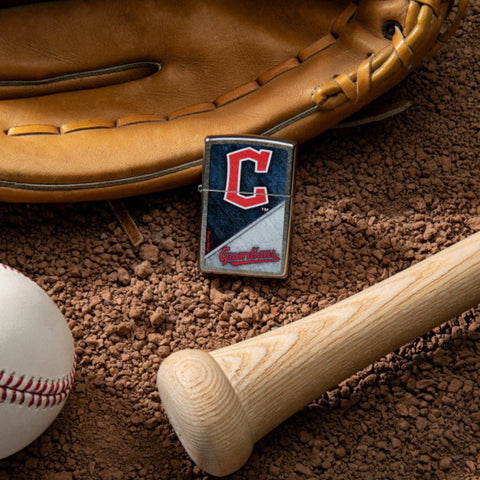 Lifestyle image of MLB® Cleveland Guardians™ Street Chrome™ Windproof Lighter laying on a baseball field with a glove, ball, and bat.