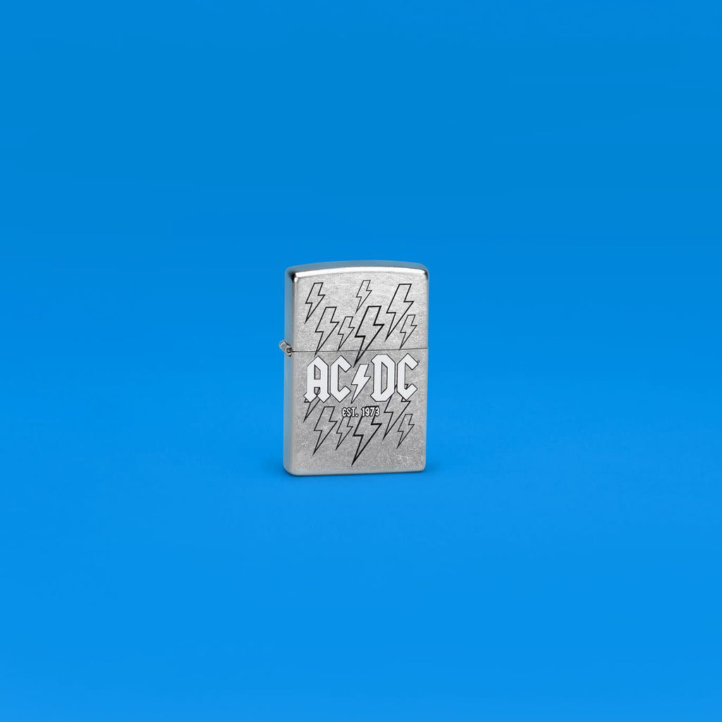 Lifestyle image of Zippo AC/DC Design Street Chrome Windproof Lighter standing in a blue scene.