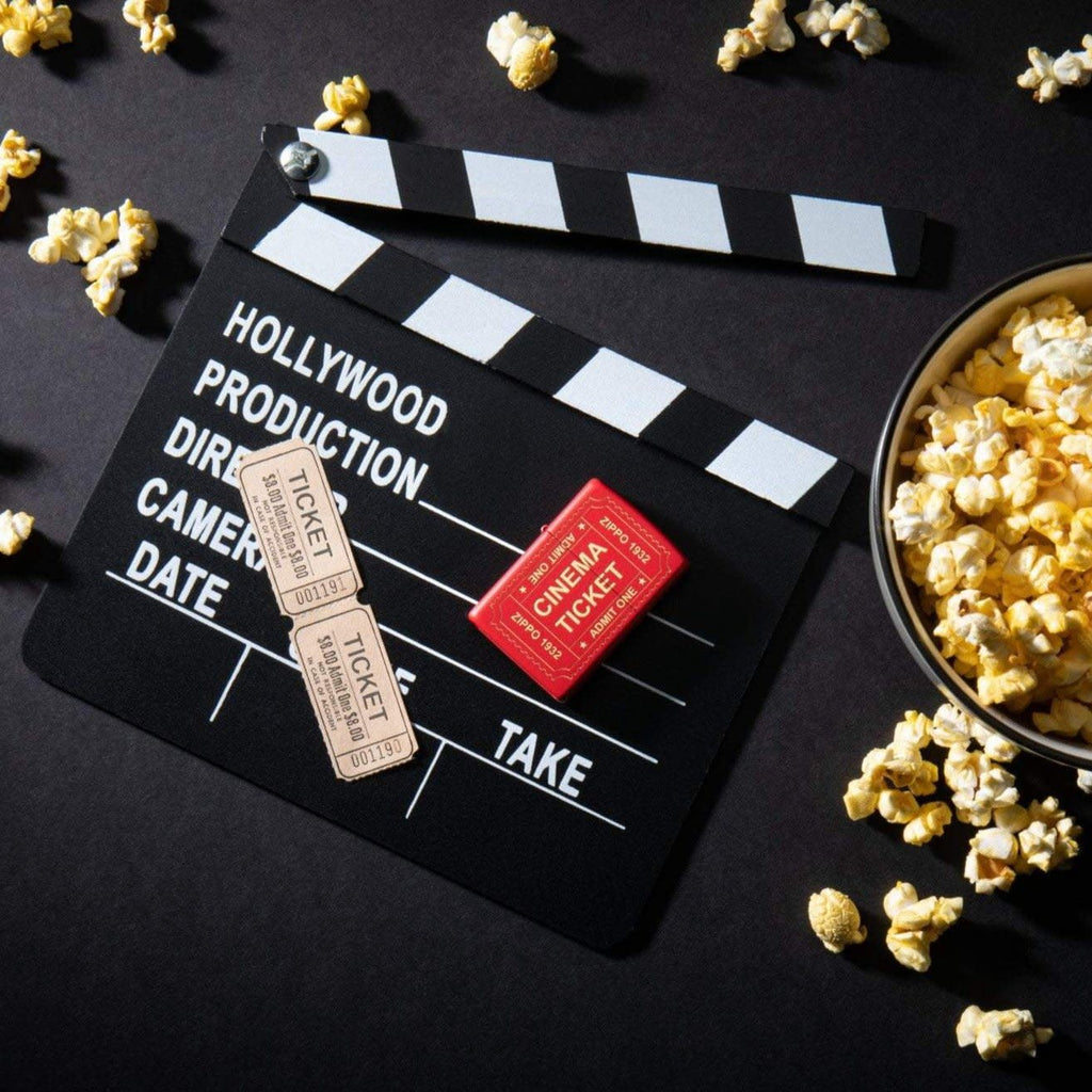 Lifestyle image of Cinema Ticket Red Matte Windproof Lighter laying on a movie clapperboard with popcorn scattered around it