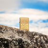 Lifestyle image of SunBeam Pendant Armor® High Polish Brass Windproof Lighter standing on a rock with clouds in the background.