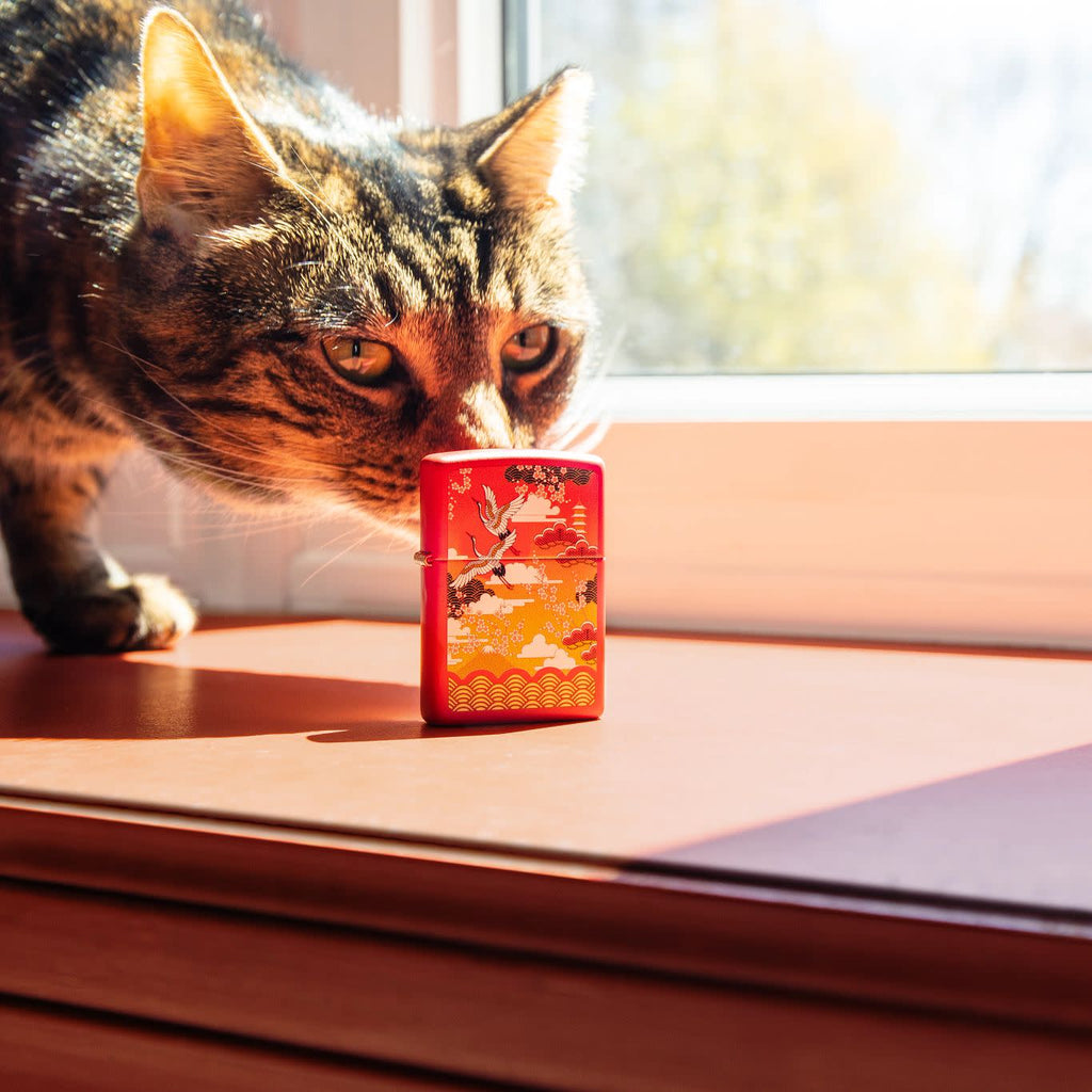 Lifestyle image of Kimono Design Red Matte Windproof Lighter standing on a window sill, with a cat behind the lighter