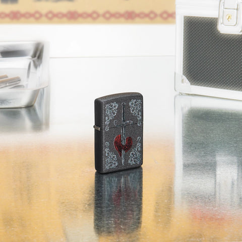 Lifestyle shot of Zippo Heart Dagger Tattoo Design Black Crackle Windproof Lighter standing in on a reflective table with tattoo equipment. 