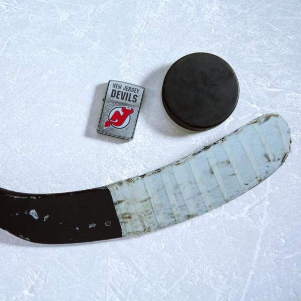 Lifestyle image of the NHL New Jersey Devilsr Street Chrome Windproof Lighter laying on ice with a hockey puck and stick